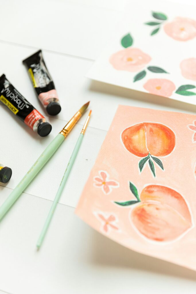 watercolor brushes and paint tubes on white background with peaches watercolor painting