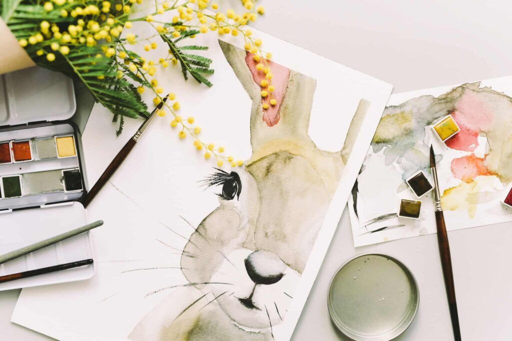 watercolor or gray rabbit with watercolor paint palette and brushes on beige background
